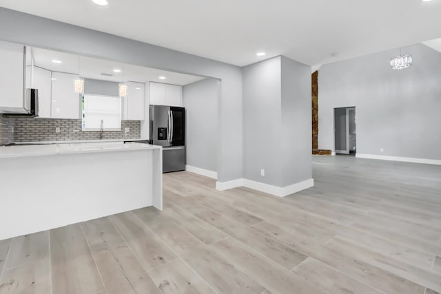 kitchen with tasteful backsplash, white cabinets, stainless steel fridge with ice dispenser, decorative light fixtures, and light wood-type flooring