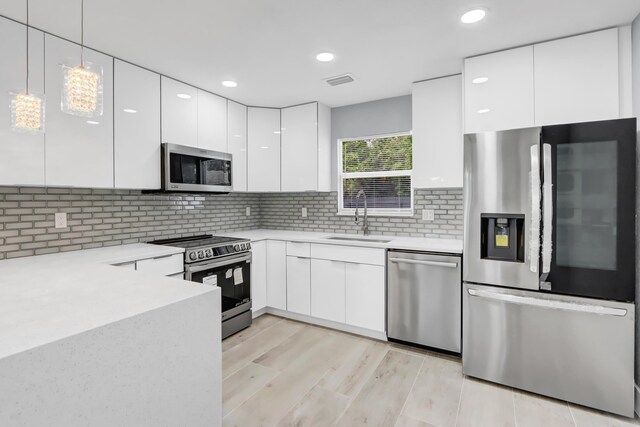 kitchen with appliances with stainless steel finishes, tasteful backsplash, white cabinetry, sink, and hanging light fixtures