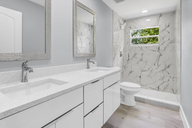 bathroom featuring a tile shower, vanity, hardwood / wood-style floors, and toilet