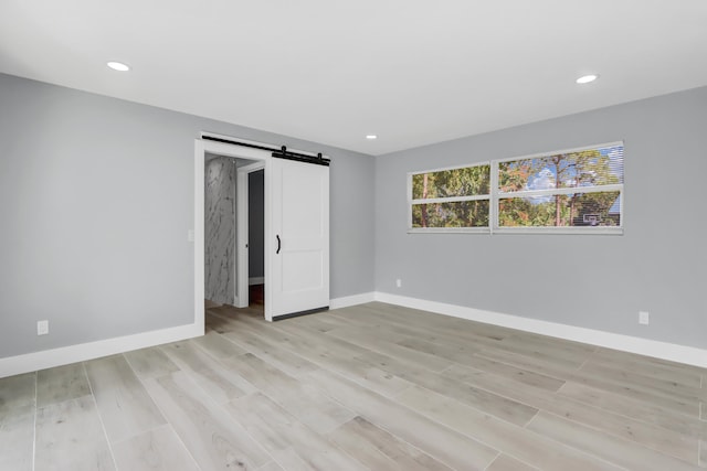 unfurnished bedroom with light hardwood / wood-style flooring and a barn door