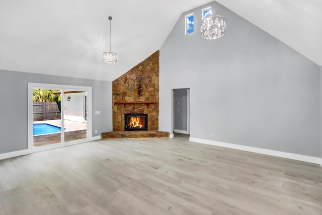 unfurnished living room featuring a stone fireplace, high vaulted ceiling, a chandelier, and light hardwood / wood-style flooring