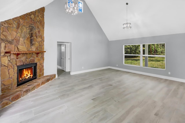 unfurnished living room featuring a stone fireplace, high vaulted ceiling, an inviting chandelier, and light hardwood / wood-style floors