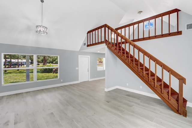 unfurnished living room with light hardwood / wood-style floors, high vaulted ceiling, and a notable chandelier