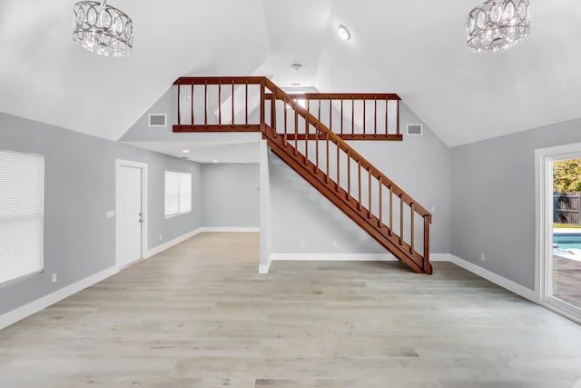 unfurnished living room with high vaulted ceiling, light wood-type flooring, and an inviting chandelier