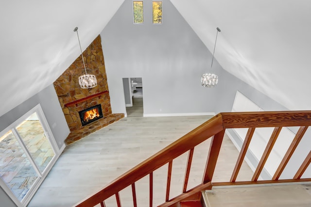 stairs with hardwood / wood-style flooring, high vaulted ceiling, a notable chandelier, and a fireplace