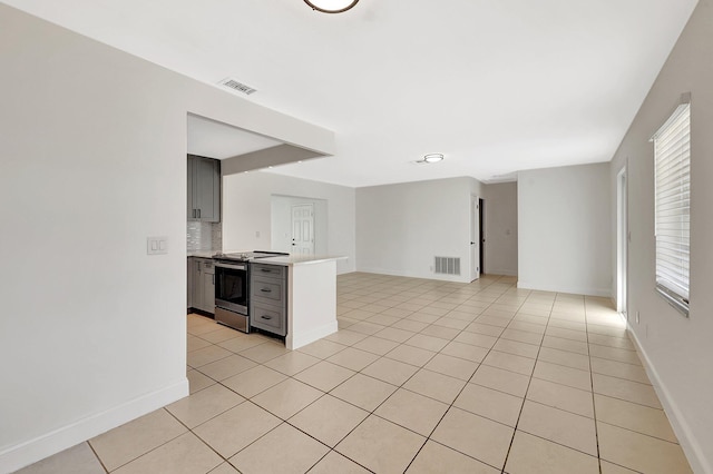 kitchen with light tile patterned floors, decorative backsplash, gray cabinets, and stainless steel range with electric cooktop