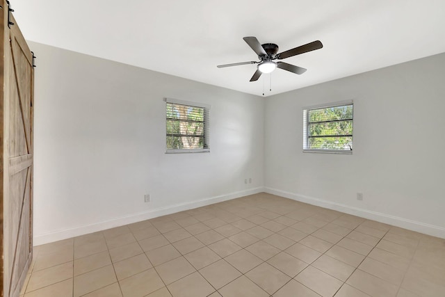 unfurnished room with ceiling fan, a barn door, and a healthy amount of sunlight