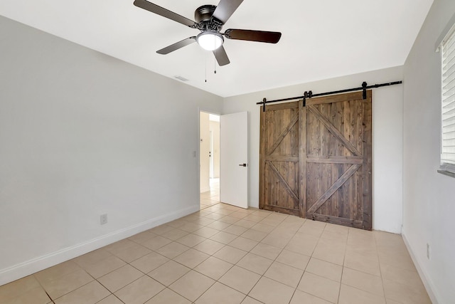 unfurnished bedroom featuring light tile patterned floors, a barn door, and ceiling fan