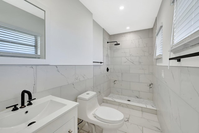 bathroom with a tile shower, vanity, tile walls, and toilet