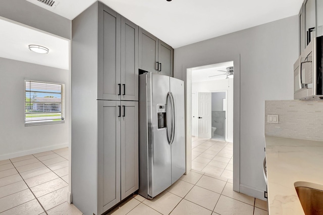 kitchen with appliances with stainless steel finishes, gray cabinetry, decorative backsplash, light tile patterned floors, and ceiling fan