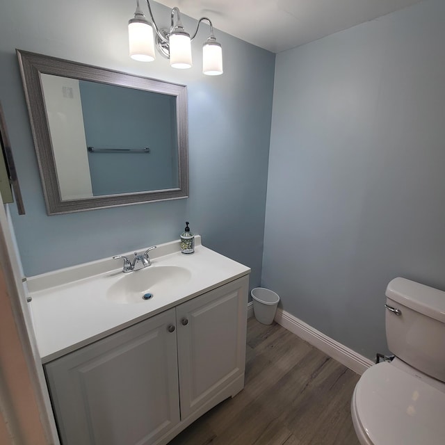 half bath with toilet, baseboards, wood finished floors, and vanity