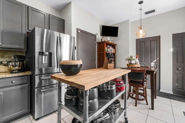 kitchen with hanging light fixtures, light tile patterned floors, stainless steel fridge, and light stone counters