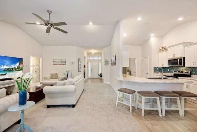 living room with ceiling fan, high vaulted ceiling, light hardwood / wood-style floors, and sink