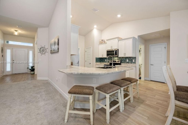 kitchen featuring a kitchen breakfast bar, light hardwood / wood-style floors, white cabinets, decorative backsplash, and vaulted ceiling