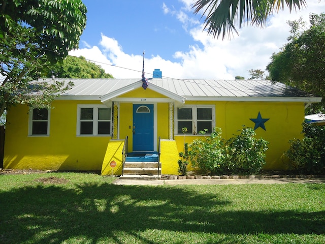 bungalow featuring metal roof, a chimney, a front lawn, and stucco siding