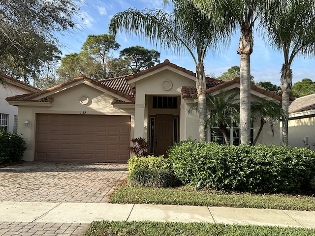 mediterranean / spanish-style house featuring a garage, a tiled roof, decorative driveway, and stucco siding