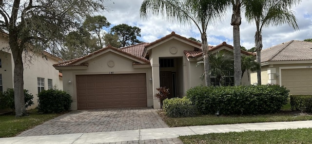 mediterranean / spanish-style home featuring decorative driveway, an attached garage, a tile roof, and stucco siding