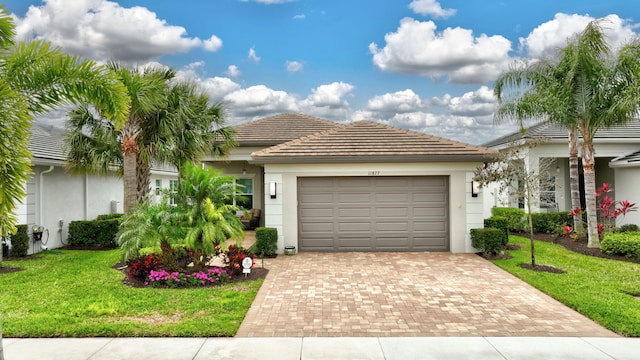 view of front facade featuring a garage, a tiled roof, decorative driveway, stucco siding, and a front yard