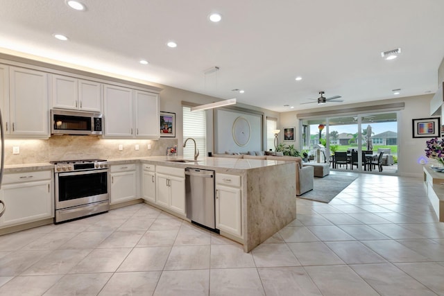 kitchen featuring light tile patterned flooring, a peninsula, a sink, open floor plan, and appliances with stainless steel finishes