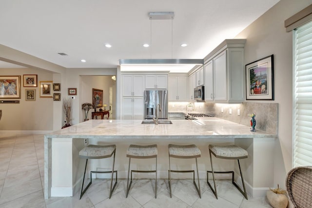 kitchen with backsplash, appliances with stainless steel finishes, a kitchen breakfast bar, a peninsula, and baseboards