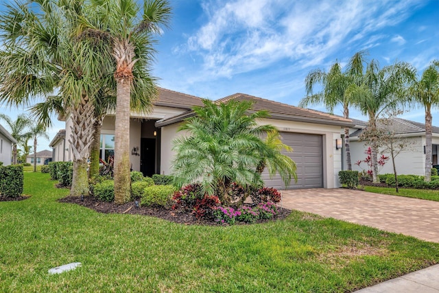 view of front of property with decorative driveway, a tile roof, stucco siding, a garage, and a front lawn