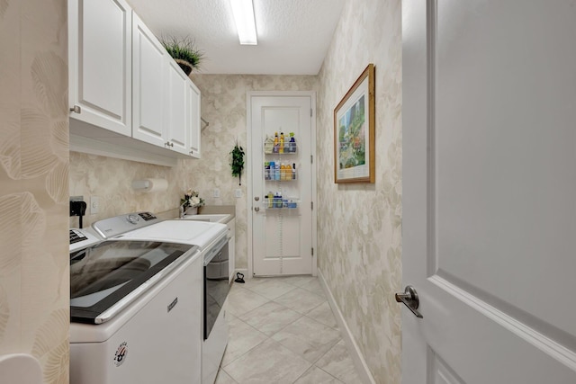 washroom with cabinet space, a sink, a textured ceiling, independent washer and dryer, and wallpapered walls