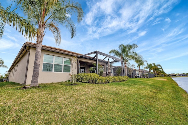 rear view of property featuring glass enclosure, a lawn, and stucco siding