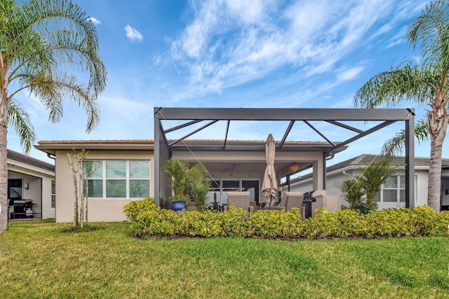 rear view of house with glass enclosure, a ceiling fan, a lawn, and stucco siding