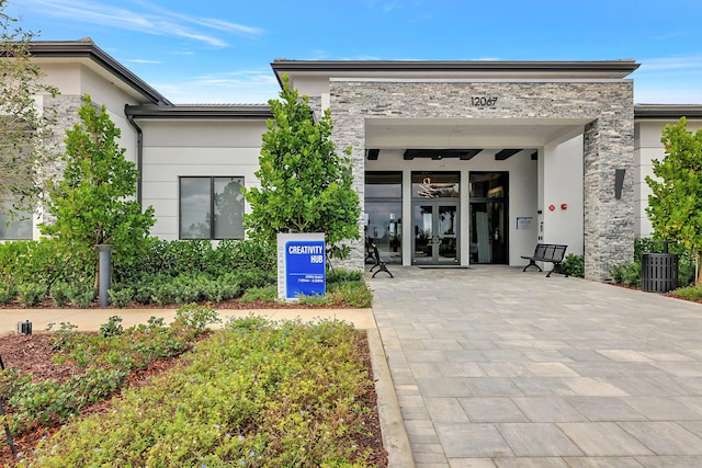 view of exterior entry with stucco siding, stone siding, and french doors