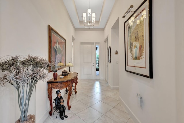 foyer entrance with light tile patterned floors, a tray ceiling, an inviting chandelier, and baseboards