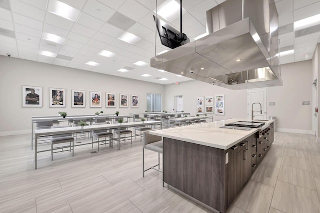 kitchen with light stone counters, stainless steel gas cooktop, a large island, a breakfast bar area, and dark brown cabinetry