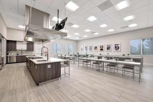 kitchen with dark brown cabinetry, an island with sink, modern cabinets, island exhaust hood, and light countertops