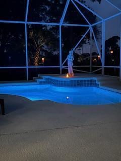 pool at twilight with a patio area and glass enclosure