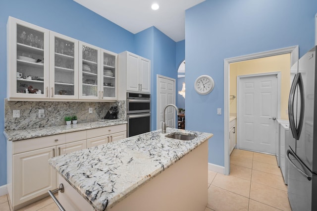 kitchen featuring light tile patterned floors, sink, stainless steel appliances, light stone countertops, and a center island with sink