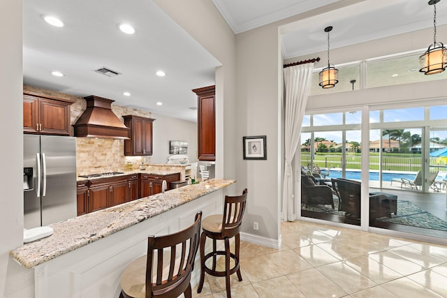 kitchen featuring custom exhaust hood, light stone countertops, appliances with stainless steel finishes, and a breakfast bar area