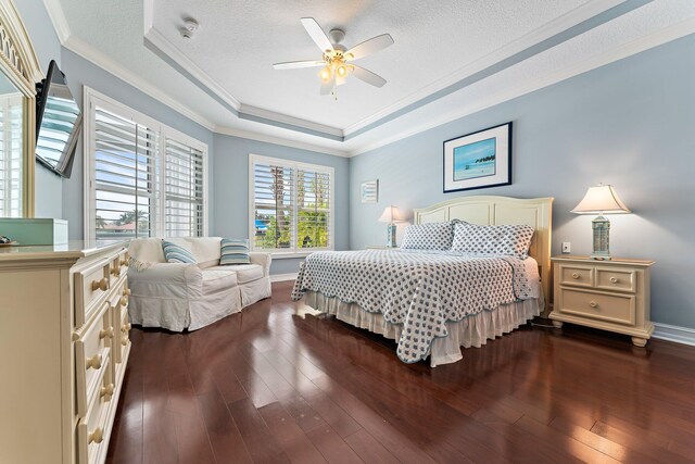 bedroom featuring dark wood-type flooring, ceiling fan, ornamental molding, a textured ceiling, and a raised ceiling