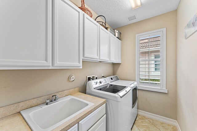 laundry room featuring light tile patterned flooring, sink, cabinets, separate washer and dryer, and a textured ceiling