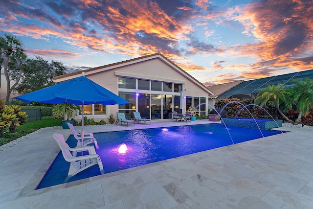 pool at dusk featuring pool water feature and a patio area