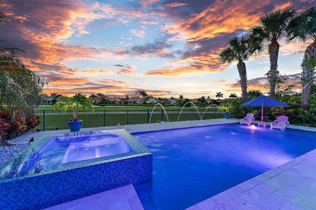 pool at dusk featuring pool water feature and an in ground hot tub