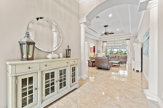 hall with ornamental molding, a tray ceiling, and ornate columns