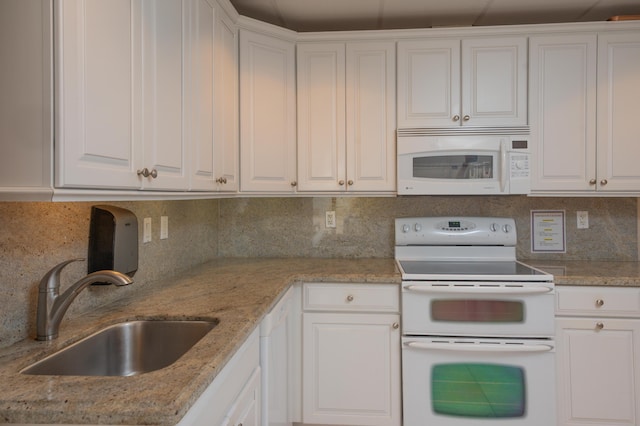 kitchen featuring white appliances, white cabinetry, light stone counters, and a sink