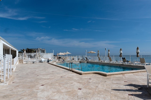 community pool with a patio area, fence, and a water view