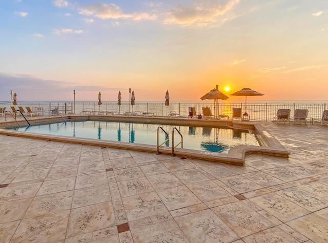 pool with a patio area, a water view, and fence