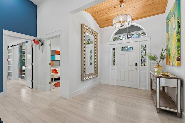 foyer with light hardwood / wood-style flooring, an inviting chandelier, high vaulted ceiling, wooden ceiling, and a barn door