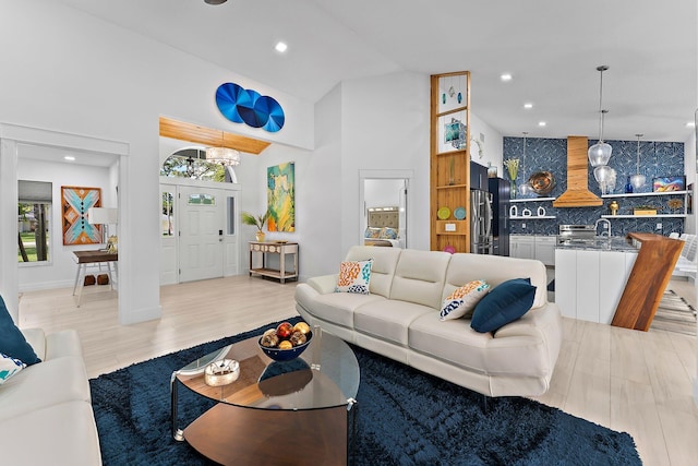 living room with high vaulted ceiling, light hardwood / wood-style floors, and sink