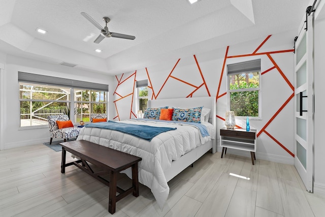 bedroom featuring multiple windows, a barn door, a textured ceiling, and a tray ceiling