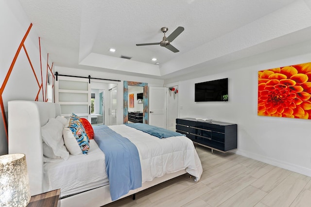 bedroom with ceiling fan, a tray ceiling, a barn door, and a textured ceiling