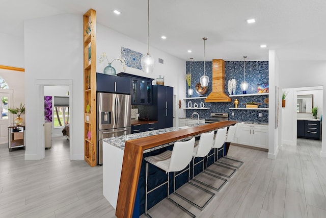 kitchen featuring premium range hood, stainless steel appliances, decorative backsplash, a kitchen bar, and decorative light fixtures