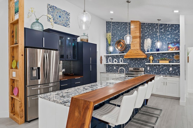 kitchen featuring blue cabinets, hanging light fixtures, dark stone counters, custom range hood, and stainless steel appliances