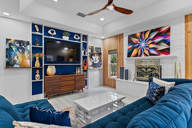 living room featuring hardwood / wood-style flooring, a tile fireplace, ceiling fan, and wood walls